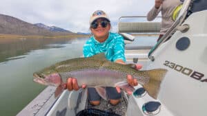 A fly fisherman holding a large rainbow trout in a boat on Crowley Lake near Mammoth Lakes, CA