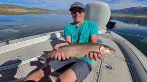 A fly fisherman holding a large cuthhroat trout in a boat on Crowley Lake near Mammoth Lakes, CA