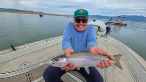 A fly fisherman holding a large rainbow trout in a boat on Crowley Lake near Mammoth Lakes, CA