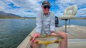 A fly fisherman holding a large brown trout in a boat on Crowley Lake near Mammoth Lakes, CA