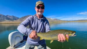 A fly fisherman holding a large brown trout in a boat on Crowley Lake near Mammoth Lakes, CA