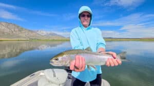 A fly fisherman holding a large rainbow trout in a boat on Crowley Lake near Mammoth Lakes, CA