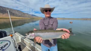 A fly fisherman holding a large rainbow trout in a boat on Crowley Lake near Mammoth Lakes, CA