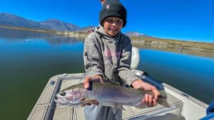 A fly fisherman holding a large rainbow trout in a boat on Crowley Lake near Mammoth Lakes, CA