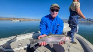 A fly fisherman holding a large rainbow trout in a boat on Crowley Lake near Mammoth Lakes, CA