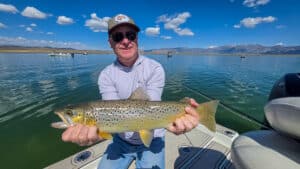 A fly fisherman holding a large brown trout in a boat on Crowley Lake near Mammoth Lakes, CA