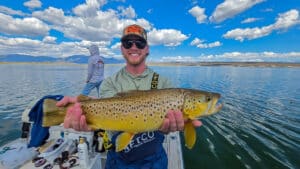A fly fisherman holding a large brown trout in a boat on Crowley Lake near Mammoth Lakes, CA