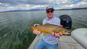 A fly fisherman holding a large brown trout in a boat on Crowley Lake near Mammoth Lakes, CA