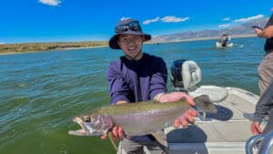 A fly fisherman holding a large rainbow trout in a boat on Crowley Lake near Mammoth Lakes, CA