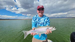 A fly fisherman holding a large rainbow trout in a boat on Crowley Lake near Mammoth Lakes, CA