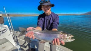 A fly fisherman holding a large rainbow trout in a boat on Crowley Lake near Mammoth Lakes, CA