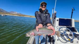 A fly fisherman holding a large rainbow trout in a boat on Crowley Lake near Mammoth Lakes, CA