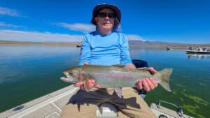 A fly fisherman holding a large rainbow trout in a boat on Crowley Lake near Mammoth Lakes, CA