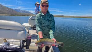 A fly fisherman holding a large rainbow trout in a boat on Crowley Lake near Mammoth Lakes, CA