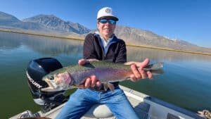 A fly fisherman holding a large rainbow trout in a boat on Crowley Lake near Mammoth Lakes, CA