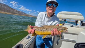 A fly fisherman holding a large brown trout in a boat on Crowley Lake near Mammoth Lakes, CA