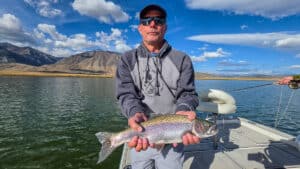 A fly fisherman holding a large rainbow trout in a boat on Crowley Lake near Mammoth Lakes, CA