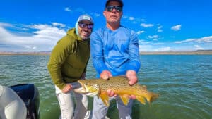 A fly fisherman holding a large brown trout in a boat on Crowley Lake near Mammoth Lakes, CA