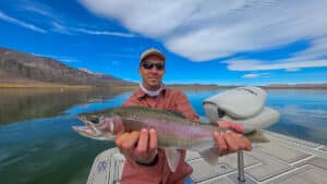 A fly fisherman holding a large rainbow trout in a boat on Crowley Lake near Mammoth Lakes, CA