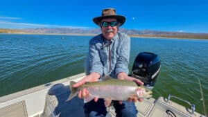 A fly fisherman holding a large rainbow trout in a boat on Crowley Lake near Mammoth Lakes, CA