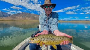 A fly fisherman holding a large brown trout in a boat on Crowley Lake near Mammoth Lakes, CA