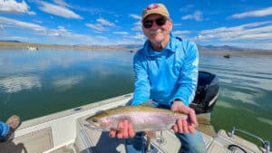 A fly fisherman holding a large rainbow trout in a boat on Crowley Lake near Mammoth Lakes, CA