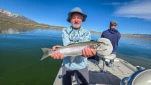 A fly fisherman holding a large rainbow trout in a boat on Crowley Lake near Mammoth Lakes, CA