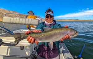 A fly fisherman holding a large rainbow trout in a boat on Crowley Lake near Mammoth Lakes, CA