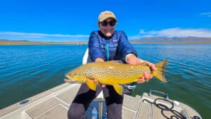 A fly fisherman holding a large brown trout in a boat on Crowley Lake near Mammoth Lakes, CA