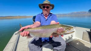 A fly fisherman holding a large rainbow trout in a boat on Crowley Lake near Mammoth Lakes, CA