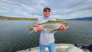 A fly fisherman holding a large rainbow trout in a boat on Crowley Lake near Mammoth Lakes, CA