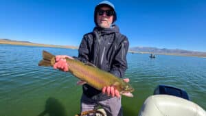 A fly fisherman holding a large cuthhroat trout in a boat on Crowley Lake near Mammoth Lakes, CA