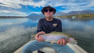 A fly fisherman holding a large rainbow trout in a boat on Crowley Lake near Mammoth Lakes, CA