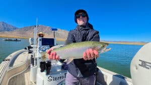 A fly fisherman holding a large rainbow trout in a boat on Crowley Lake near Mammoth Lakes, CA