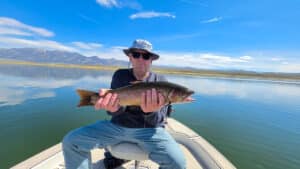 A fly fisherman holding a large cuthhroat trout in a boat on Crowley Lake near Mammoth Lakes, CA