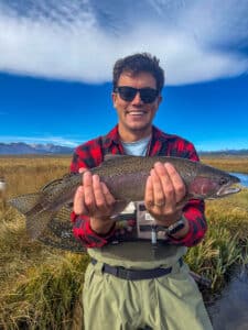 A fly fisherman holding a large rainbow trout in the Upper Owens River near Mammoth Lakes, CA