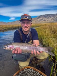 A fly fisherman holding a large rainbow trout in the Upper Owens River near Mammoth Lakes, CA
