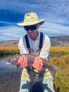 A fly fisherman holding a large rainbow trout in the Upper Owens River near Mammoth Lakes, CA
